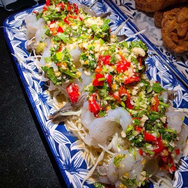 Raw shrimp with spicy green and red chili sauce, served on shredded cabbage on a blue and white plate.