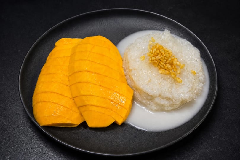 Mango sticky rice dessert with sliced mango, sticky rice, coconut milk, and golden crispy mung beans.